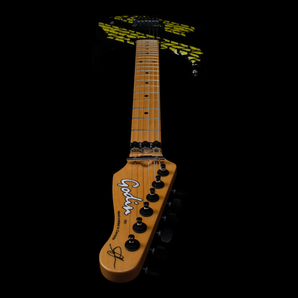 A black Godin guitar with a yellow tire tread mark graphics.