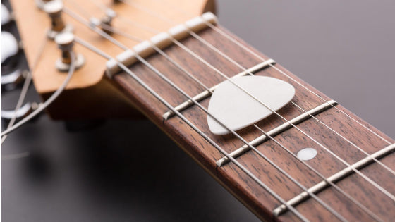 guitar pick stored under strings at the 2nd fret