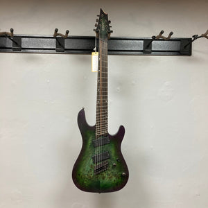 Cort KX507 SDG 7-String Multi-Scale Star Dust Green Electric Guitar hanging on a hook.