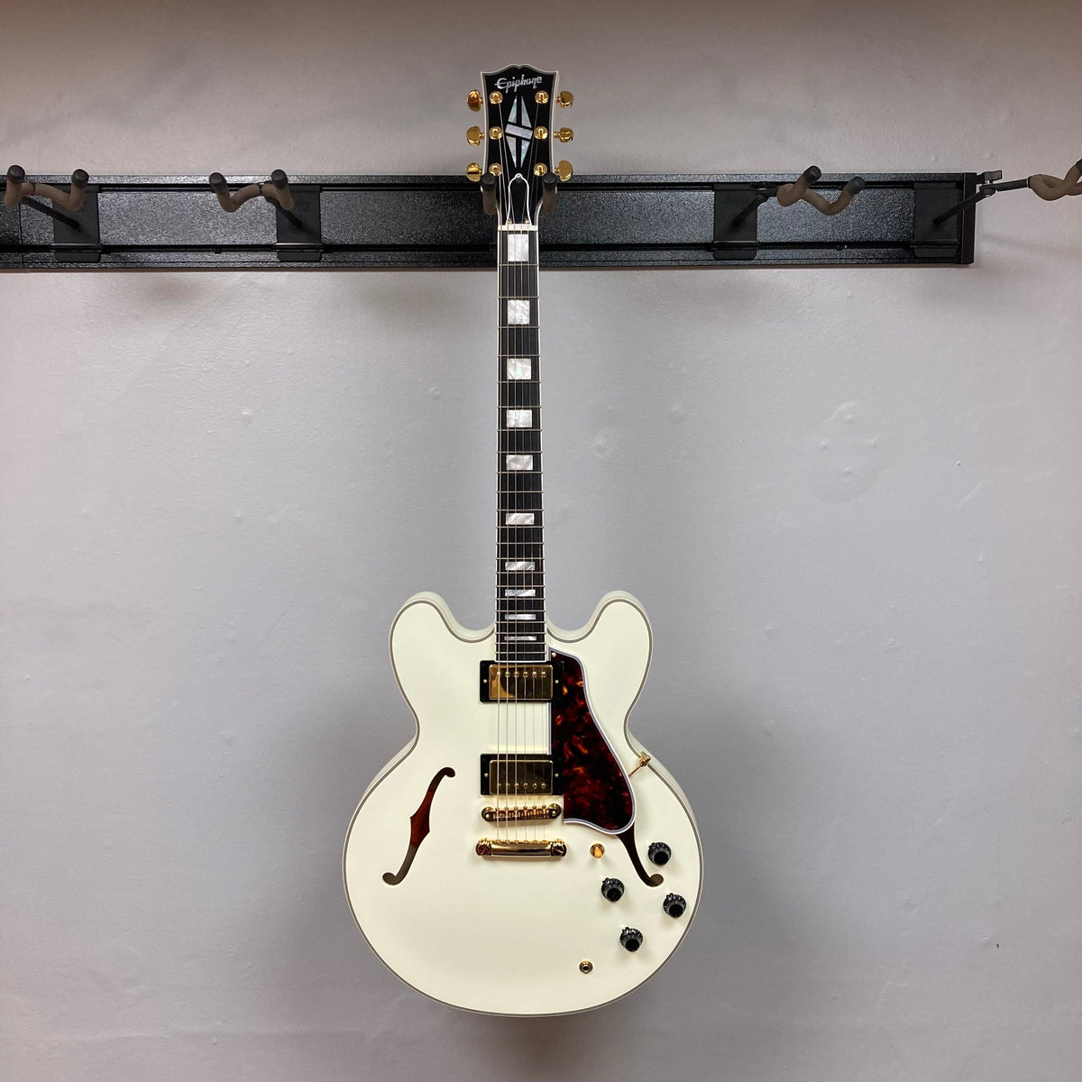 Epiphone IGC 1959 ES-355 Classic White Electric Guitar with black strings, brown and black knobs, mounted on a wall.