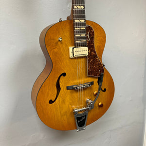 Godin 5th Avenue Jumbo P-Rail Harvest Gold guitar with archtop design, rosewood fingerboard, maple neck, and Graphtech bridge displayed on a wall.