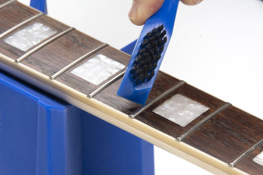 Person using a blue brush to clean a guitar, highlighting the Music Nomad Total Guitar Spa Kit for comprehensive guitar care.