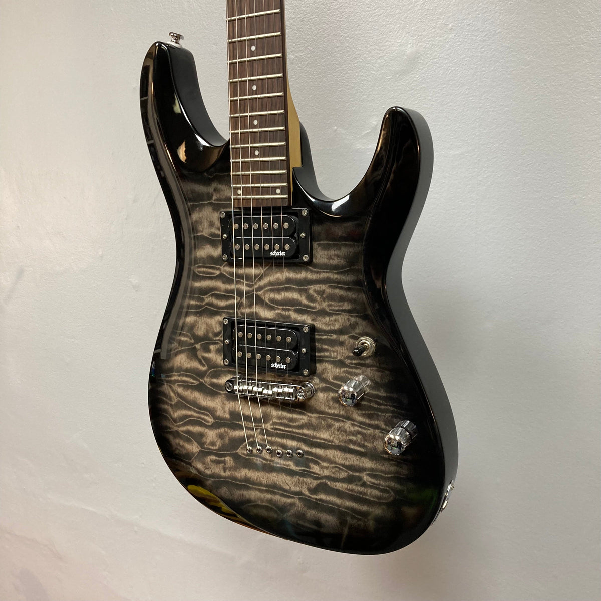 Schecter C-6 Plus Charcoal Burst Used electric guitar displayed on a wall, highlighting its strings and hardware details.