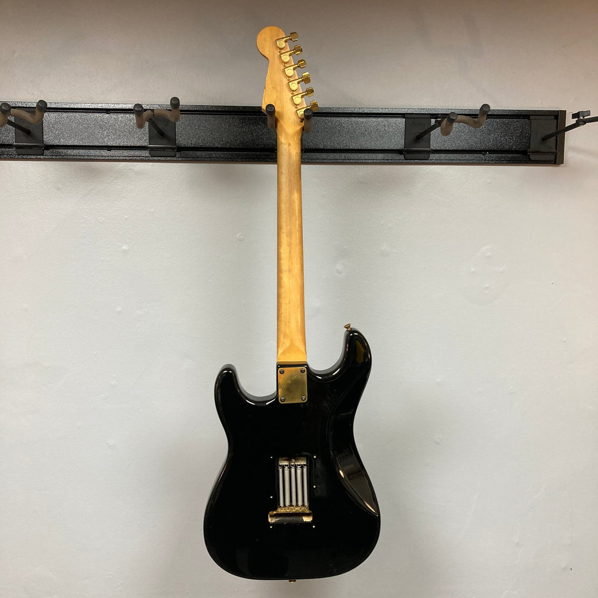 Schecter USA Super Strat, 1983-1987 Black Gold, electric guitar with distinct gold neck and detailed craftsmanship, hanging on a wall.