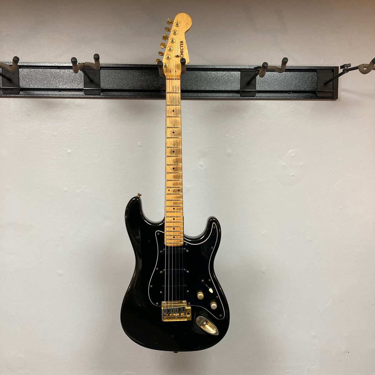 Schecter USA Super Strat 1983-1987 Black Gold electric guitar with gold hardware, displayed on a wall.