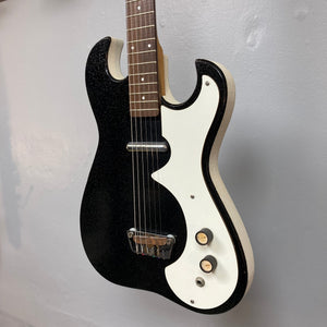 Sears Silvertone 1448 1960s Black Sparkle guitar on a wall, showcasing its compact design and single pickup.