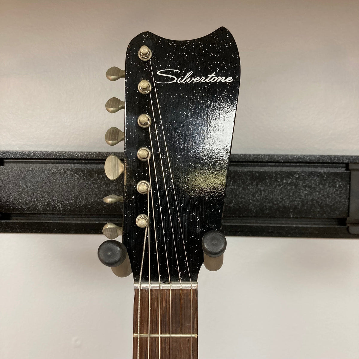 Sears Silvertone 1448 1960s Black Sparkle guitar on a stand, featuring a solid body and bolt-on neck, with a case that doubles as a portable amplifier.