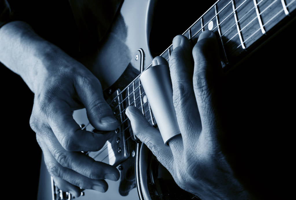 A closeup of a guitar being played using a slide