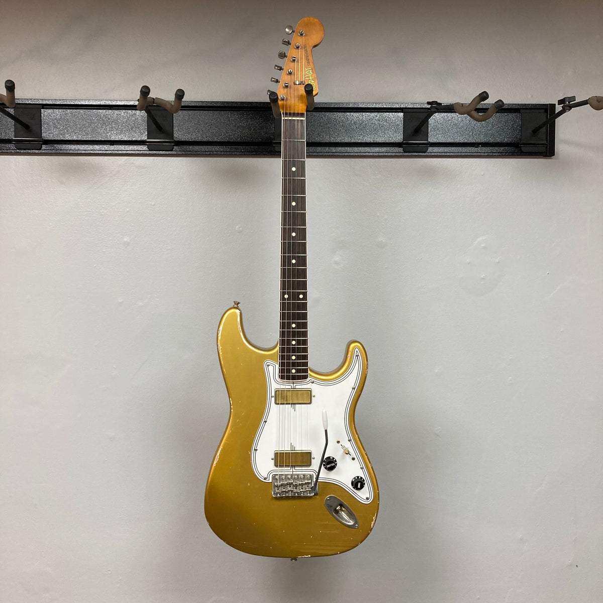 TopHat Stratavarius Aztec Gold Relic electric guitar with a signature, displayed on a wall. Features aged finish, tremolo bridge, and Gotoh tuners.