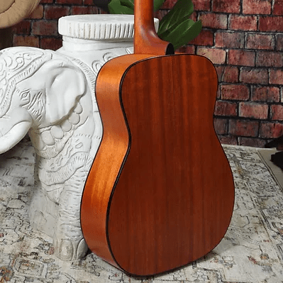 Bodhi BG10M African Okoume Mahogany Top Concert Body Acoustic Guitar, leaning against a statue, showcasing its compact and elegant design.