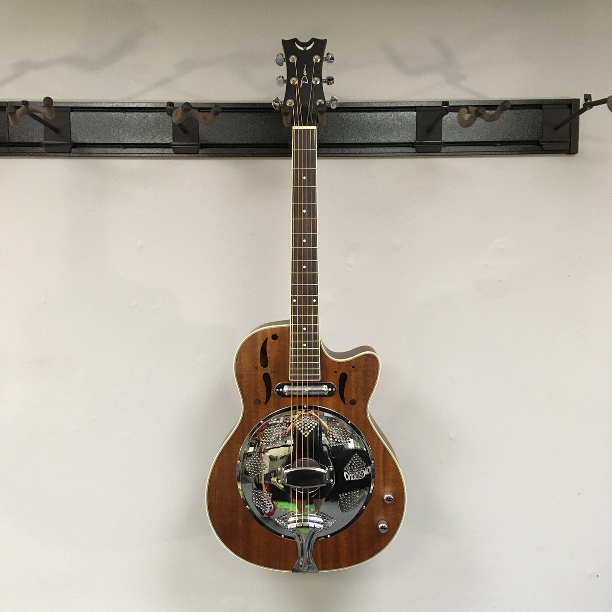 Dean CE Acoustic-Electric Resonator Guitar with eastern mahogany body, cutaway design, and 21 fret purple heart fingerboard, displayed on a wall.