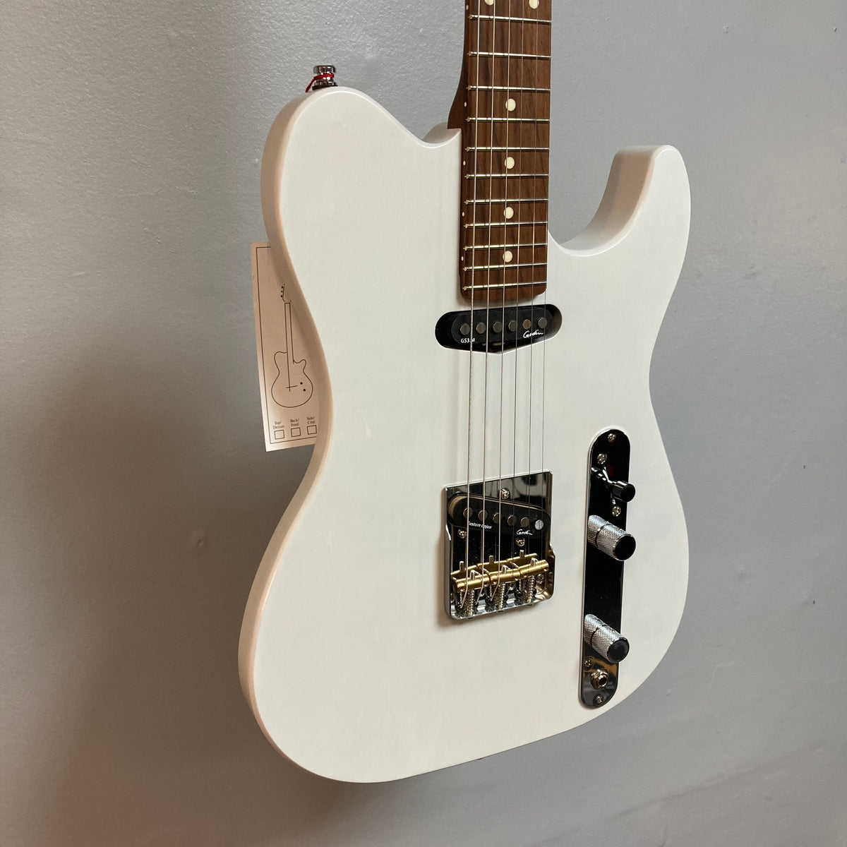 Godin Stadium HT Trans White electric guitar, featuring a sleek maple neck and custom pickups, displayed on a wall.