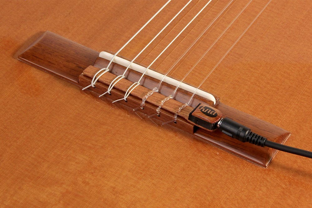 Close-up of KNA NG-1 Piezo Pick-up installed on a classical guitar&#39;s tie bar, showcasing its secure fit and elegant mahogany casing.