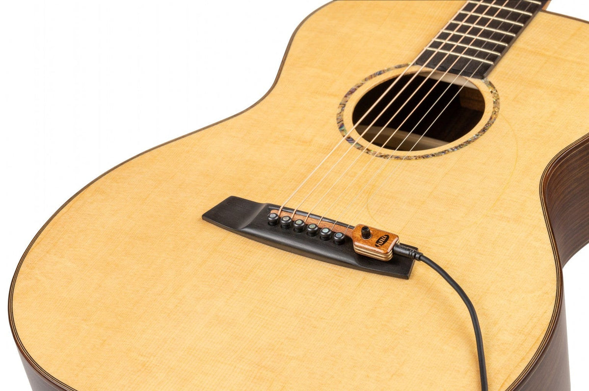 KNA SG-2 Portable Piezo Pickup for Steel String Guitar with Volume Control, shown close-up on an acoustic guitar&#39;s bridge, highlighting its integration without modifications.