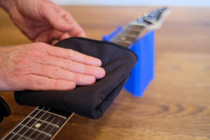 Person cleaning a guitar with MusicNomad 2 'n 1 Beyond Plush Players Cloth, highlighting its use for professional-grade instrument care and polishing.