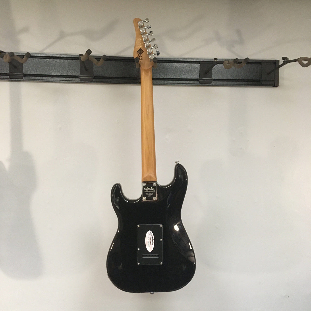 Schecter Nick Johnston Traditional Atomic Ink Open Box electric guitar displayed on a wall, featuring a roasted maple neck and chrome hardware.