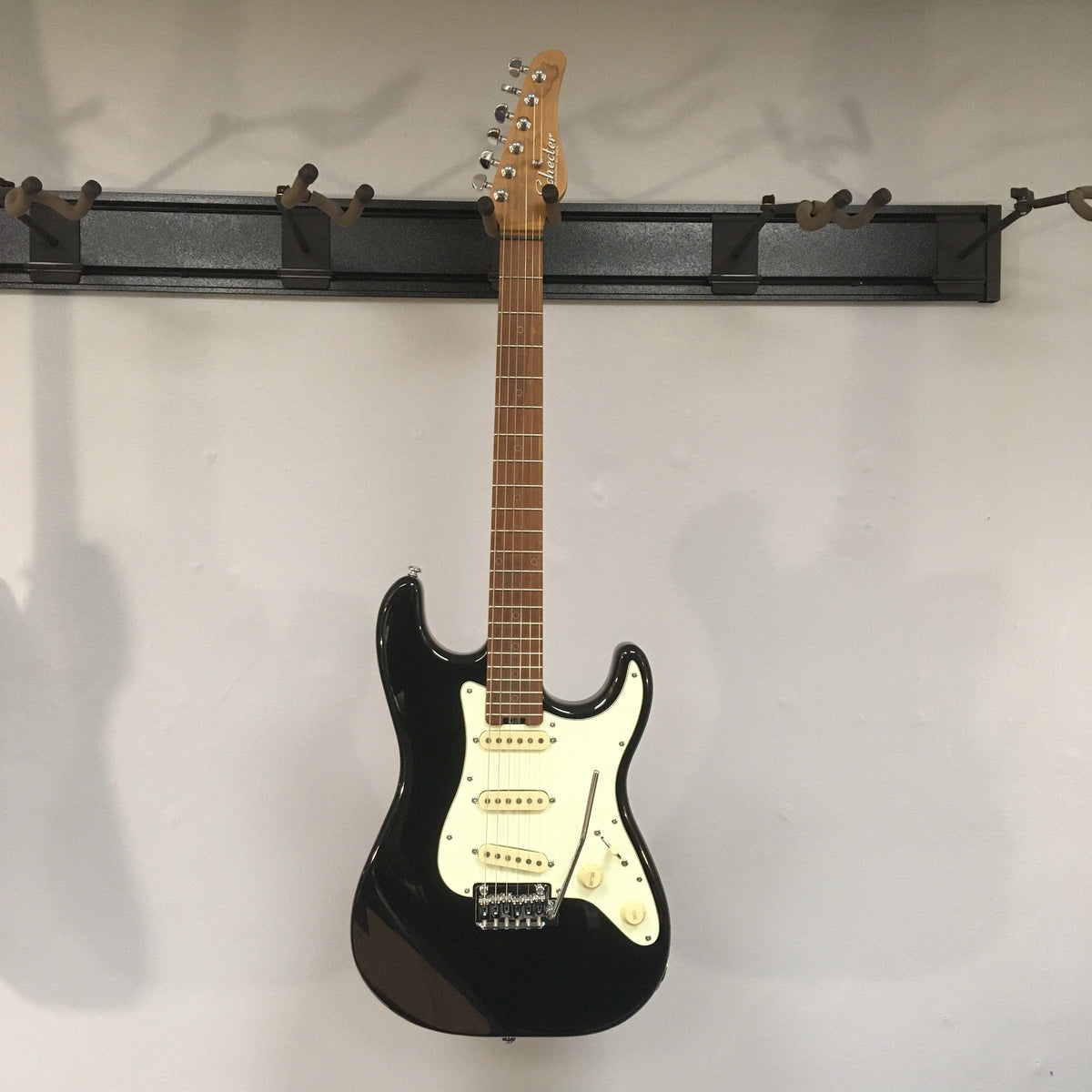 Schecter Nick Johnston Traditional Atomic Ink electric guitar with roasted maple neck, 22 frets, and vintage tremolo bridge displayed on a wall.