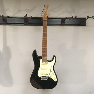 Schecter Nick Johnston Traditional Atomic Ink electric guitar with roasted maple neck, 22 frets, and vintage tremolo bridge displayed on a wall.