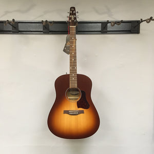 Seagull Entourage Autumn Burst Acoustic Guitar with black label hanging on a wall, showcasing its dreadnought shape and detailed craftsmanship.